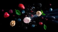 Fresh berries, macarons, and mint leaves floating in dark space with water splashes and drops creating dynamic food composition on black background.