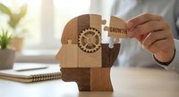 Business professional assembling wooden puzzle pieces forming human head with gear mechanism, representing personal development and growth mindset concept.