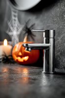 Modern chrome faucet with Halloween decorations in background, including carved pumpkin, candles, and spiderweb on dark surface.