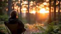 Young woman hiker with backpack watching golden sunset through forest trees, peaceful outdoor adventure and nature connection moment for wellness and travel.