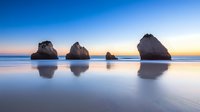 Tranquil seascape with limestone rock formations reflected in smooth water during sunrise, creating mirror-like symmetry on wet sand beach. Perfect for travel themes.