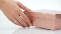 Hand reaching for elegant pink gift box on white surface, perfect for special occasions and celebrations.