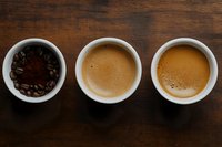 Coffee preparation stages in white cups on wooden background - roasted beans with ground coffee and two freshly brewed espressos showing rich crema.