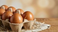 Fresh brown chicken eggs in cardboard carton on rustic wooden table with natural lighting for organic farm produce and healthy cooking concepts.