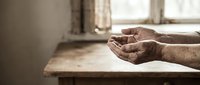 Elderly hands cupped in prayer or meditation gesture on wooden table near window, expressing faith, hope, spirituality and peaceful contemplation in warm natural light.