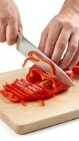 Caucasian male hands slicing fresh red bell pepper on wooden cutting board with chef knife, healthy cooking preparation concept.