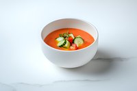 Fresh gazpacho soup garnished with cucumber and cherry tomatoes served in white ceramic bowl on marble background, cold summer appetizer.