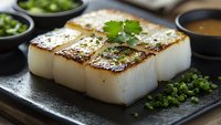 Seared sea scallops with caramelized golden-brown crust garnished with fresh herbs and green onions, served on black stone plate with dipping sauce.