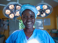 African American female healthcare professional in surgical scrubs and cap smiling confidently in operating room with surgical lights overhead, representing medical career success.