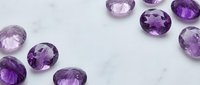 Collection of purple amethyst gemstones in various shades scattered on white marble surface for jewelry design and luxury accessories projects.
