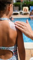 Woman applying sunscreen lotion to child's shoulder at poolside for sun protection and skin care during summer vacation.