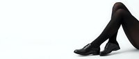 Slender female legs in black opaque tights and classic lace-up oxford shoes, posed gracefully on white background, fashion and style concept.