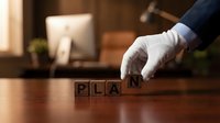 Business professional in white gloves arranging wooden letter blocks spelling PLAN on office desk for strategic planning and goal setting concepts.