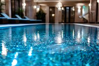 Luxurious indoor swimming pool with crystal clear turquoise water and soft lighting reflections creating a serene spa atmosphere. Blue lounge chairs visible in background.