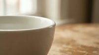 Empty white ceramic bowl on wooden table with soft natural lighting and blurred background for kitchen and dining concepts.