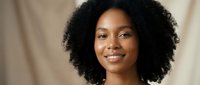 Young African American woman with natural curly hair smiling warmly at camera in soft indoor lighting for lifestyle and portrait photography.
