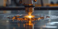 CNC laser cutting machine in operation with bright orange flame and water reflection during metal fabrication process in industrial workshop.