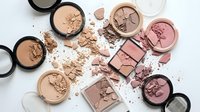 Broken makeup cosmetics powder foundation blush eyeshadow scattered on white background. Beauty products damage concept for fashion industry advertising.