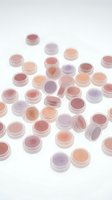 Assorted cosmetic loose pigments and mineral eyeshadows in pink, peach, purple and mauve shades displayed in clear plastic containers on white background for makeup and beauty product advertising.