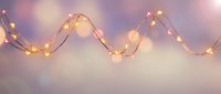 Warm glowing string lights creating elegant curves against soft purple and pink gradient background for festive decoration and ambient lighting design.