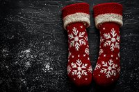 Red knitted winter socks with white snowflake pattern on dark background with snow texture. Cozy Christmas holiday mood for seasonal greeting cards.