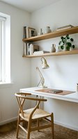Minimalist home office corner with wooden floating shelves, white desk, natural wood chair, brass task lamp, potted plant, and books for workspace organization and interior design inspiration.