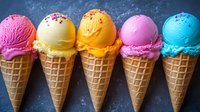 Colorful ice cream scoops in waffle cones arranged in row showing variety of flavors including strawberry, vanilla, mango, raspberry and blue mint against dark background.