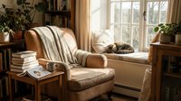 Cozy reading nook with leather armchair, books, coffee cup and sleeping cat by sunny window. Warm home interior with plants and natural light.