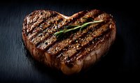 Grilled heart-shaped beef steak with rosemary sprig on dark slate background, juicy meat with charred grill marks and seasoning, close up food photography.