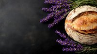 Rustic artisan bread loaf surrounded by fresh lavender sprigs on dark background, perfect for food photography or culinary marketing.