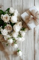 Elegant white rose bouquet with baby's breath next to gift box with beige ribbon on rustic wooden background for wedding or anniversary.