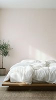 Minimalist bedroom interior with unmade white linen bedding on wooden platform bed, potted olive plant, neutral wall, and natural sunlight for home decor and lifestyle design.