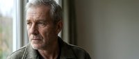 Senior man with gray hair and facial hair, appearing contemplative while gazing out window in natural light, suitable for healthcare, aging, lifestyle and editorial content.