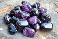 Polished amethyst stones scattered on rustic surface showing deep purple and violet hues with natural crystalline patterns and smooth tumbled texture.