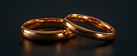 Two elegant gold wedding bands on dark background with soft reflection, classic minimalist design showcasing eternal commitment and matrimonial symbolism.