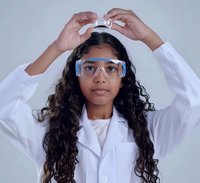 Young South Asian female scientist in lab coat adjusting protective goggles against light gray background, representing STEM education and research.