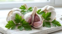 Fresh garlic bulbs and cloves with green parsley leaves arranged on rustic wooden cutting board in bright kitchen setting for cooking and culinary use.