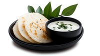 South Indian steamed rice cakes with coconut chutney on black plate, traditional breakfast dish with fresh curry leaves garnish isolated on white background.