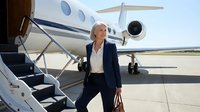 Mature woman in business attire descending aircraft stairs on tarmac, private jet in background, corporate travel and executive lifestyle concept.