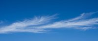Clear blue sky with wispy white clouds stretching across horizon on sunny day for nature backgrounds and weather concepts.
