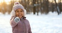 Happy young girl in winter clothing enjoying snowy day outdoors with warm sunlight creating magical atmosphere for seasonal family activities.