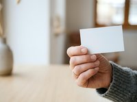 Close-up of hand holding blank white card in modern office setting, suitable for branding, business presentations, and corporate marketing materials.