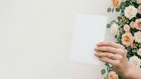 Woman holding blank white card next to peach roses and eucalyptus greenery for wedding invitations, greeting cards, or event announcements.