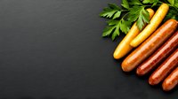 Fresh grilled sausages arranged diagonally with parsley leaves on dark slate background, copy space for menu or recipe text.