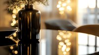 Elegant black glass vase with delicate branches against golden bokeh lights creating luxurious ambiance. Reflective surface adds depth and sophistication to modern home decor setting.