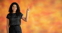 Young Hispanic woman with curly hair pointing upward in black casual outfit against vibrant orange sunset sky background for advertising and marketing campaigns.