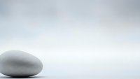 Single smooth gray zen stone on white surface with soft gradient background for meditation and wellness concepts.