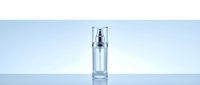 Clear glass cosmetic serum bottle with silver pump dispenser on reflective surface against light blue gradient background for skincare product packaging.