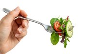 Hand holding fork with fresh mixed salad greens, cherry tomato and cucumber slice isolated on white background for healthy eating concepts.