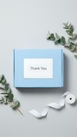 Light blue gift box with Thank You label, white ribbon, and eucalyptus branches on gray background, flat lay for packaging design.